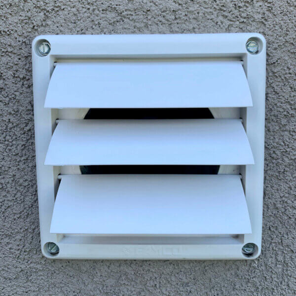 Front view of white colored FAMCO plastic wall vent with movable louvers installed into the side of a home.
