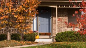 A house entrance decorated with pumpkins and surrounded by vibrant autumn foliage.