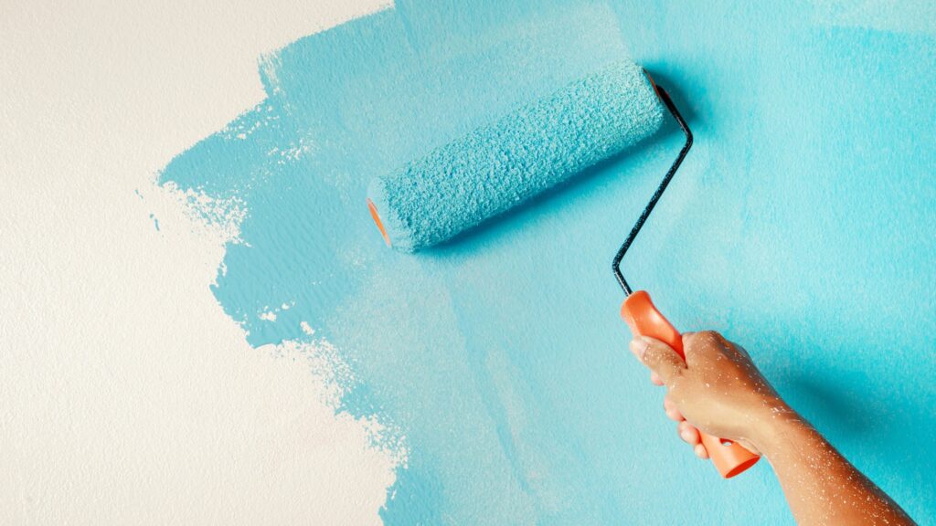 man holding roller brush painting on wall